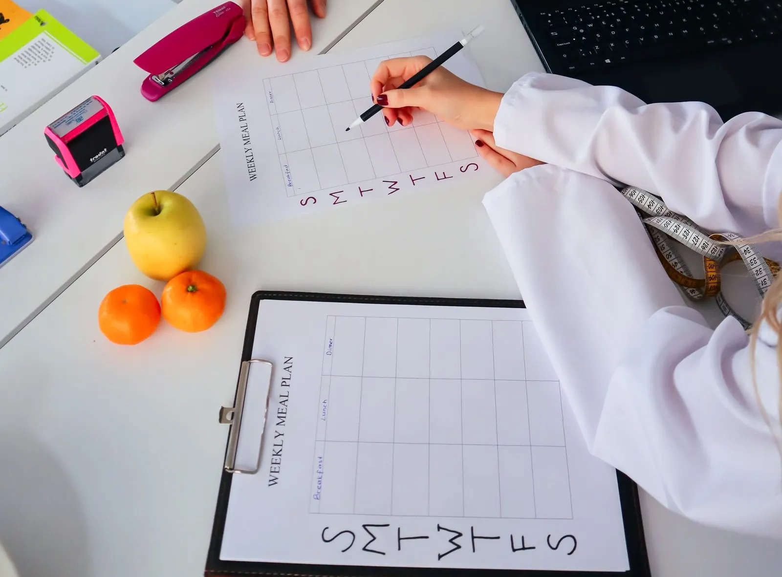 A clinician with a measuring tape writing a weekly meal plan during a nutrition consultation